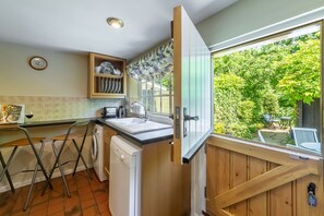 A compact kitchen with a washing machine, a sink, and a window overlooking a garden.