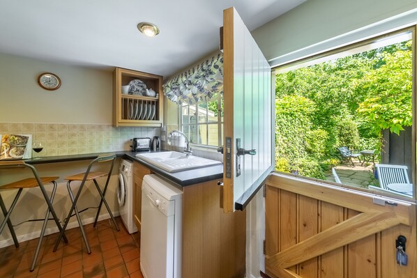 A compact kitchen with a washing machine, a sink, and a window overlooking a garden.
