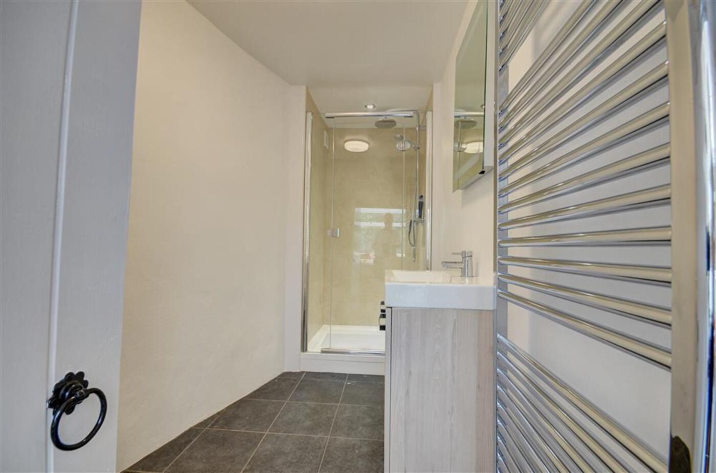 Un baño moderno con cabina de ducha de vidrio, un lavabo blanco y un perchero para toallas.