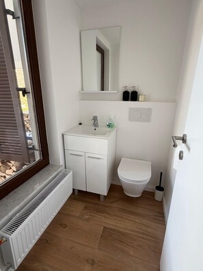 A compact bathroom with a white sink, mirror, and toilet. A radiator is under the sink, and there are toiletries on the wall.