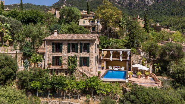 Une villa en pierre dotée d’une piscine, entourée d’une végétation luxuriante et de montagnes.