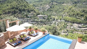 Un espace aménagé au bord de la piscine, avec des chaises longues et des parasols, offrant une vue sur un paysage montagneux parsemé de bâtiments.