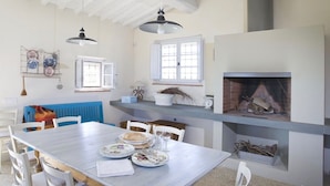 A dining area with a wooden table, chairs, a fireplace, and a window with shutters. - Breathtaking views of the Chianti hills, Tradition, Sustainability and Design (Montespertoli/Firenze)