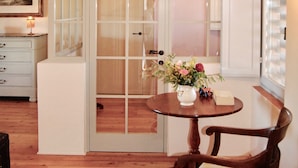 A room with a wooden floor, a white cabinet, a wooden chair with a cushion, a round table with a vase of flowers, and a sliding glass door leading to a bathroom. - Breathtaking views of the Chianti hills, Tradition, Sustainability and Design (Montespertoli/Firenze)