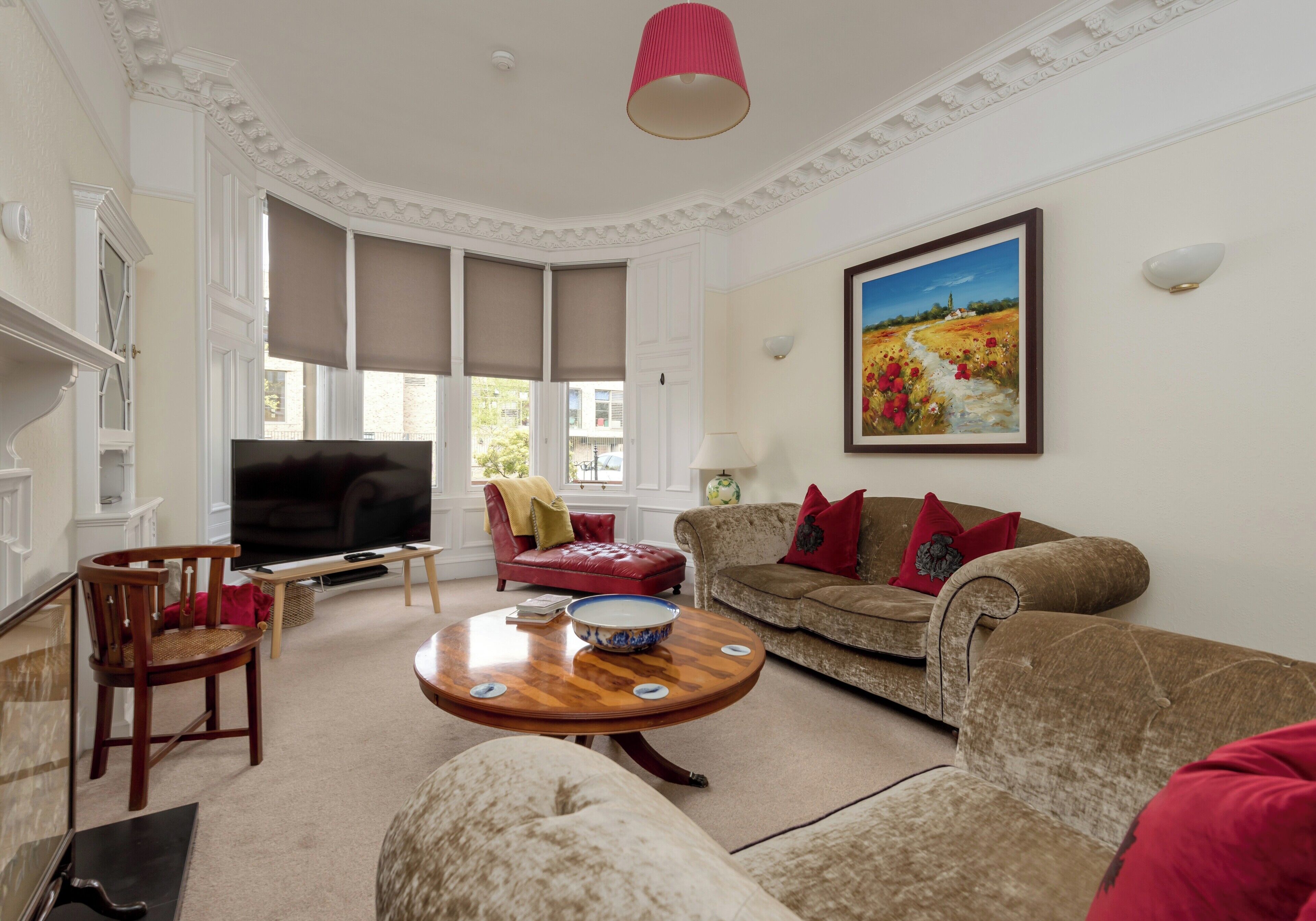 A living room with a television, a red leather chair, a brown sofa with red cushions, a wooden coffee table, and a painting on the wall.