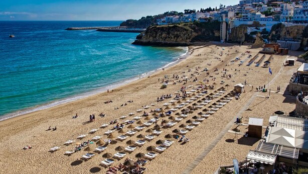 A beach with rows of sunbeds and umbrellas, a clear blue sea, and buildings in the background. - Luxury 1 Bedroom, Apartment Marina de Albufeira near Old Town (Albufeira)