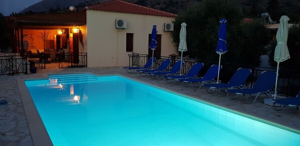 Ein Swimmingpool mit Liegestühlen und Sonnenschirmen, eine überdachte Sitzgelegenheit und ein Gebäude mit rotem Dach.