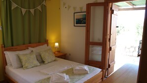 A bed with a wooden frame, a nightstand with a lamp, a green curtain, and a wooden door leading outside.