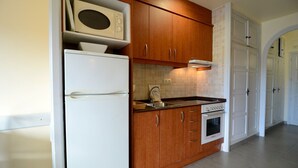 Una cucina compatta con mobili in legno, un frigorifero bianco, un forno a microonde, un fornello e un lavello.
