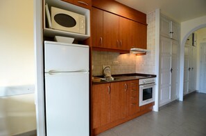 A compact kitchen with wooden cabinets, a white refrigerator, a microwave, a stove, and a sink.