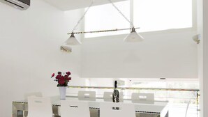 Un espace repas moderne avec une table et des chaises blanches, un luminaire suspendu et un vase rempli de fleurs.