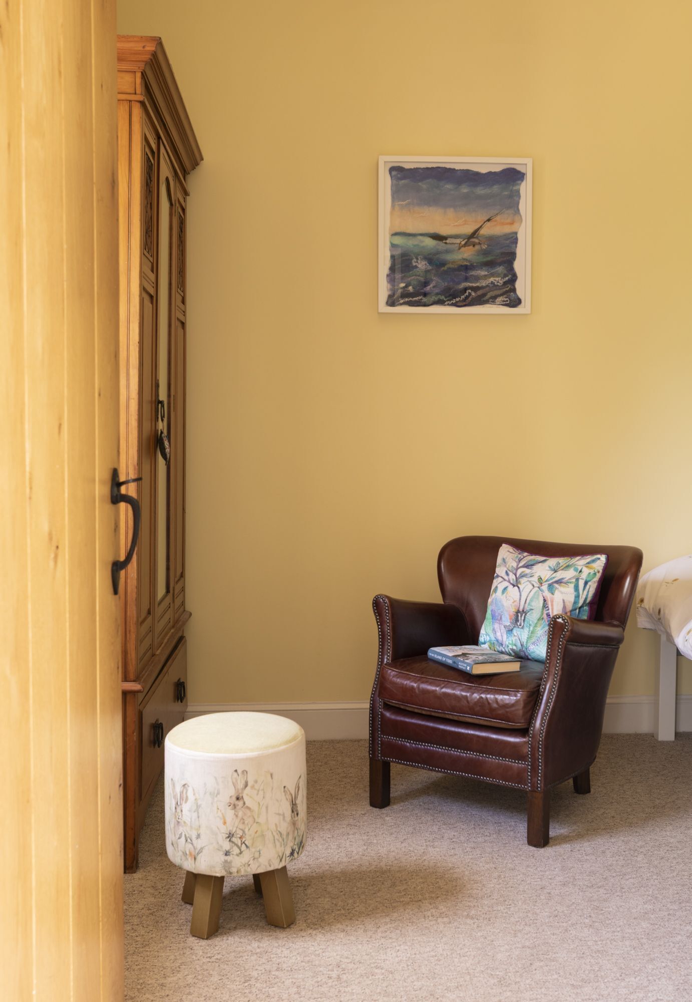A room with a wooden cabinet, a brown leather chair with a pillow, and a small round ottoman.