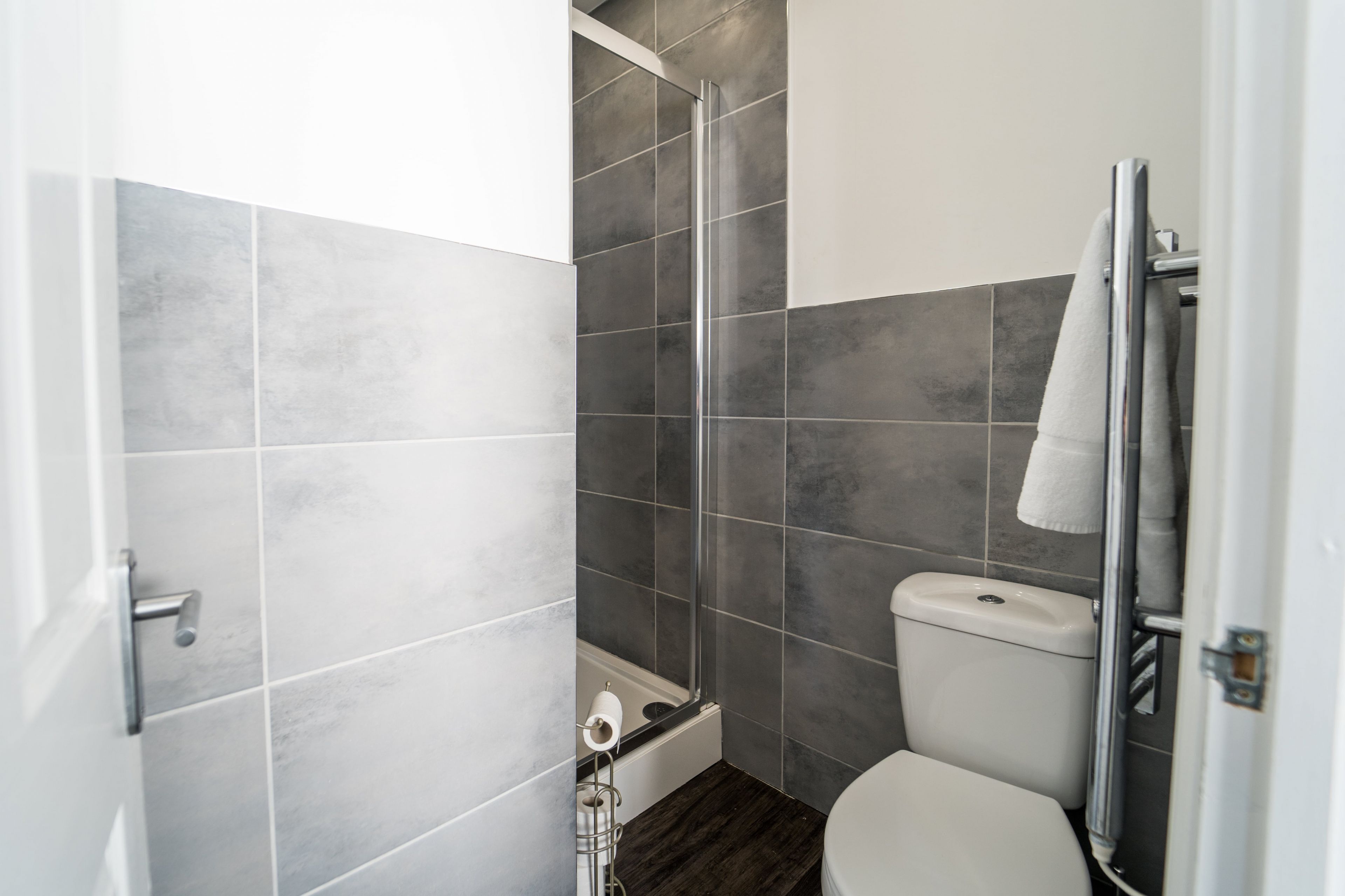 Un baño moderno con azulejos grises, cabina de ducha de cristal, inodoro y toallero.