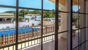 A view through a window of a pool area with a wooden fence, a clear blue sky, and buildings in the background. - Villa Borras w/ private pool, 3km to beach! (El Vendrell)
