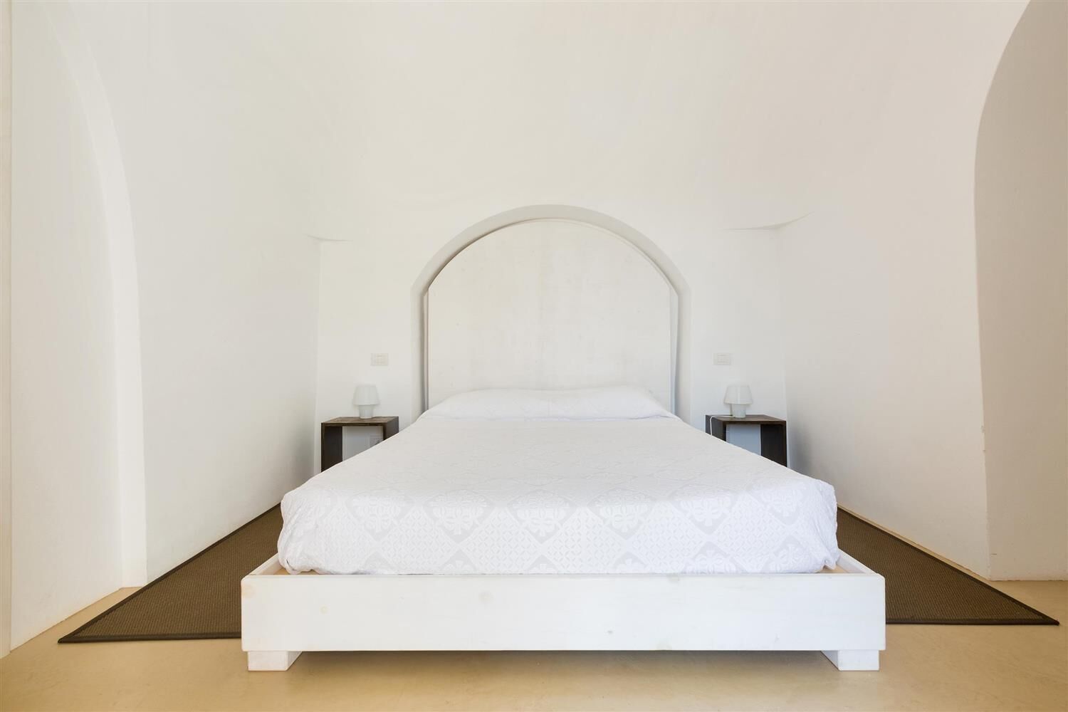 Een minimalistisch hotelkamer met een wit bed, twee nachtkastjes en een strak, eenvoudig design.