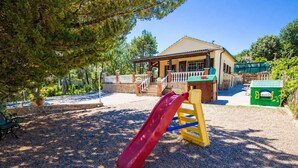 A playground with a red slide and yellow climbing structure, surrounded by trees and a building with a porch.