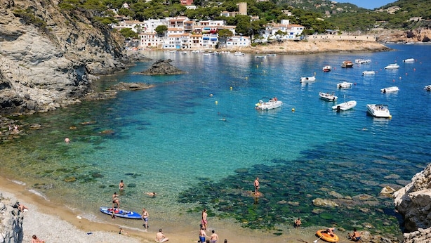 A coastal town with clear waters, boats, and people on the beach.