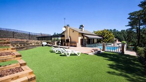 A house with a patio area, a swimming pool, and a garden with artificial grass and wooden steps.