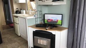 Cocina compacta con refrigerador, estufa y televisor mostrando un automóvil.