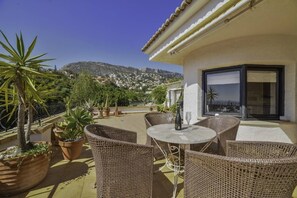 A terrace with wicker furniture, potted plants, and a view of a hillside town. - Apartment Brisa - PlusHolidays (Calpe)