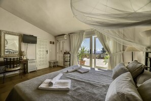 A bedroom with a bed, a desk, a television, and a view of the outdoors.