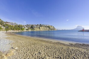 A beach with a rocky shoreline, a red lighthouse, and buildings on a hillside.