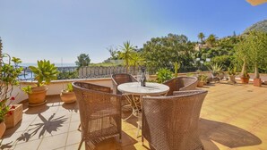 Une terrasse dotée de meubles en osier et agrémentée de plantes en pot, offrant une vue sur la côte.