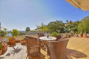 A terrace with wicker furniture and potted plants, overlooking a coastal area. - Apartment Brisa - PlusHolidays (Calpe)
