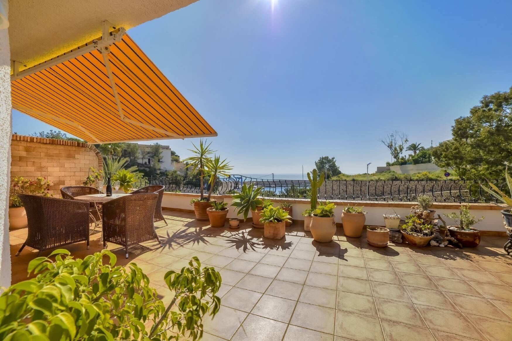 A rooftop terrace with a table and chairs, potted plants, and a view of the sea.