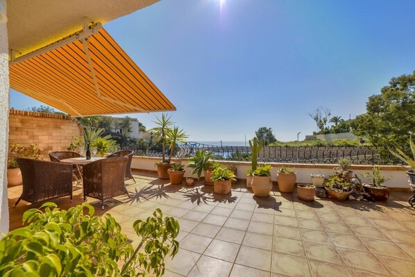 A rooftop terrace with a table and chairs, potted plants, and a view of the sea.