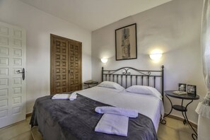 A hotel room with a bed, a wooden wardrobe, a framed picture on the wall, and a small table with a lamp. - Apartment Brisa - PlusHolidays (Calpe)