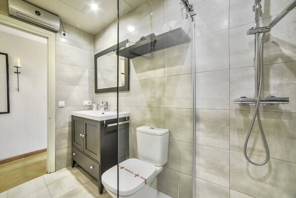 Et moderne badeværelse med glasbrusekabine, hvidt toilet og et vaskeskab med spejl.