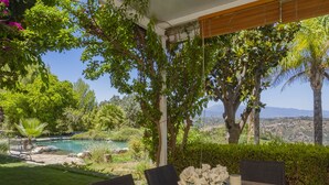 Une table en bois entourée de chaises, une bougie et un panier de fleurs, le tout mis en valeur par un jardin luxuriant en arrière-plan et une vue sur un paysage montagneux.