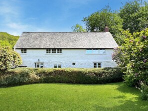 A two-story white house with a sloped roof, surrounded by a well-maintained lawn and dense shrubbery.