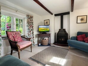 A living room with a fireplace, a television, a blue sofa, a patterned chair, and a window with curtains.