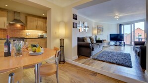 A modern living room with a sofa, a flat-screen TV, and a dining area with a table and chairs. - 2 Bed in Woolacombe (oc-narr9) (Woolacombe)