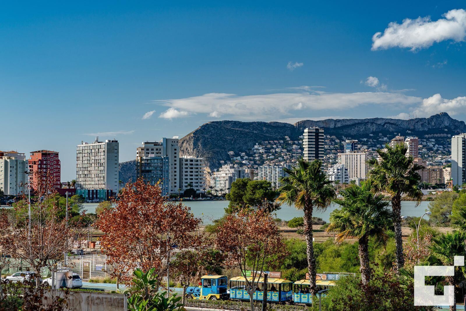 Un paysage urbain côtier avec des bâtiments modernes, un ciel dégagé et une étendue d’eau au premier plan.