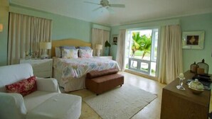 Quarto com cama, sofá, mesa de cabeceira de madeira, ventilador de teto e janela com cortinas.