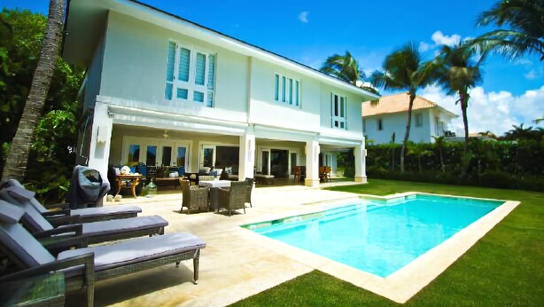 Uma casa grande com piscina, móveis de exterior e palmeiras.