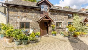 A stone building with a central entrance, multiple windows, and a paved courtyard with potted plants.