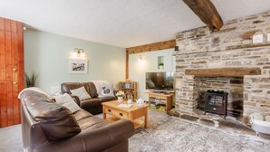 A cozy living room with a stone fireplace, leather sofas, a wooden coffee table, and a bookshelf.