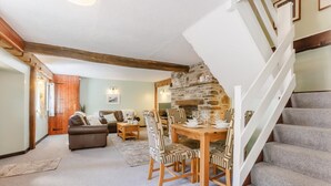 A cozy living room with a fireplace, a dining area with a wooden table and chairs, and a staircase with a white railing.