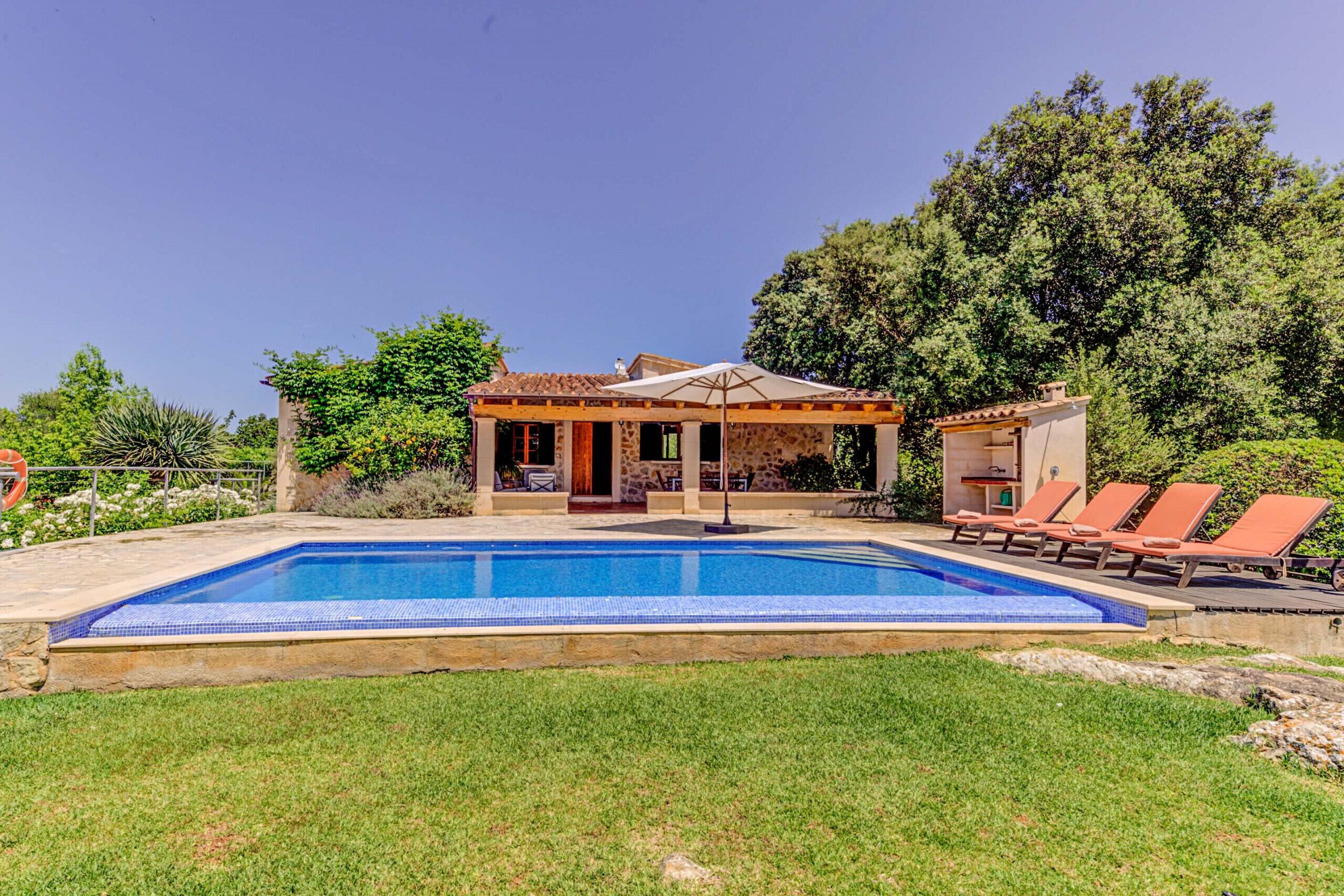 A swimming pool with a stone deck, a covered patio, and lounge chairs.