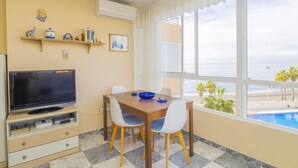 Ein Zimmer mit Fernseher, Esstisch, Stühlen und Blick auf den Strand.