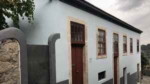A building with a light blue facade, a red door, and multiple windows with wooden frames.