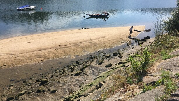 A sandy beach with a rocky shoreline, a boat on the water, and a person walking along the shore.