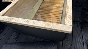 Ein Whirlpool mit einer hölzernen Sitzbank, einer Metallleitung und einem Schild mit der Aufschrift 'BATH VALVE' an einer schwarzen Holzverkleidung.