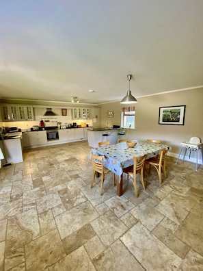 A spacious kitchen with a dining area, featuring a large island, wooden chairs, and a tiled floor.