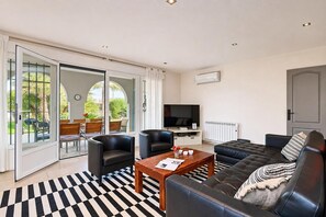 A modern living room with a sofa, two armchairs, a coffee table, and a flat-screen TV.