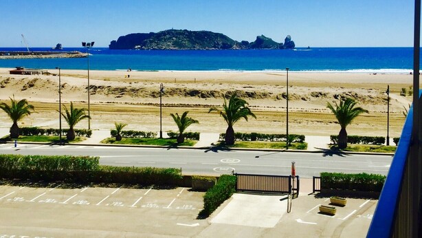 Vista de playa con una carretera al frente, palmeras y una isla en la distancia.